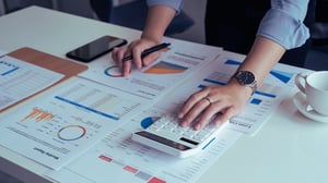 hands rest on a calculator while a person looks at their budget charts